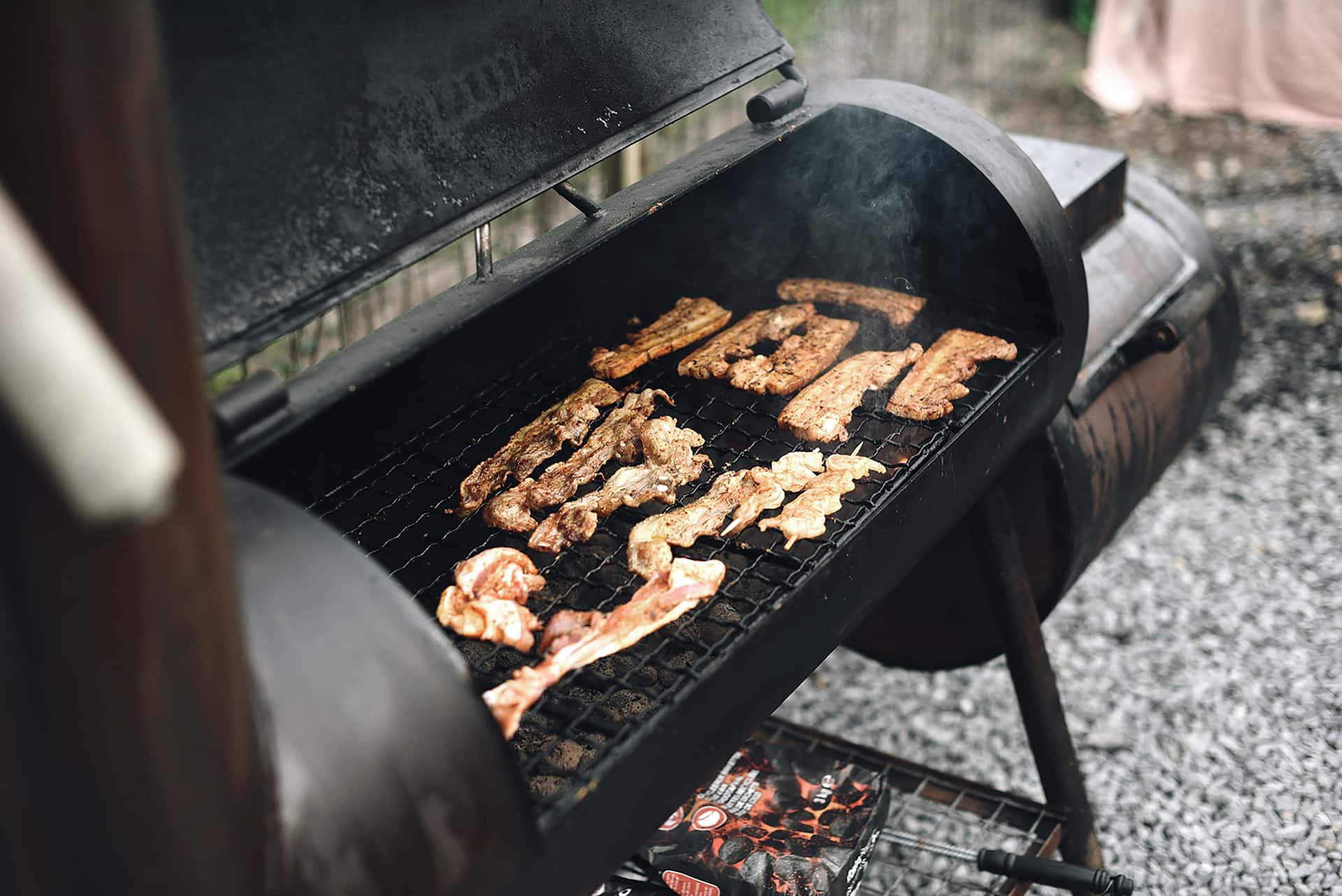 A backyard smoker with thin blue smoke rising against a muted evening sky
